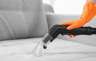 Person wearing yellow gloves vacuums a couch